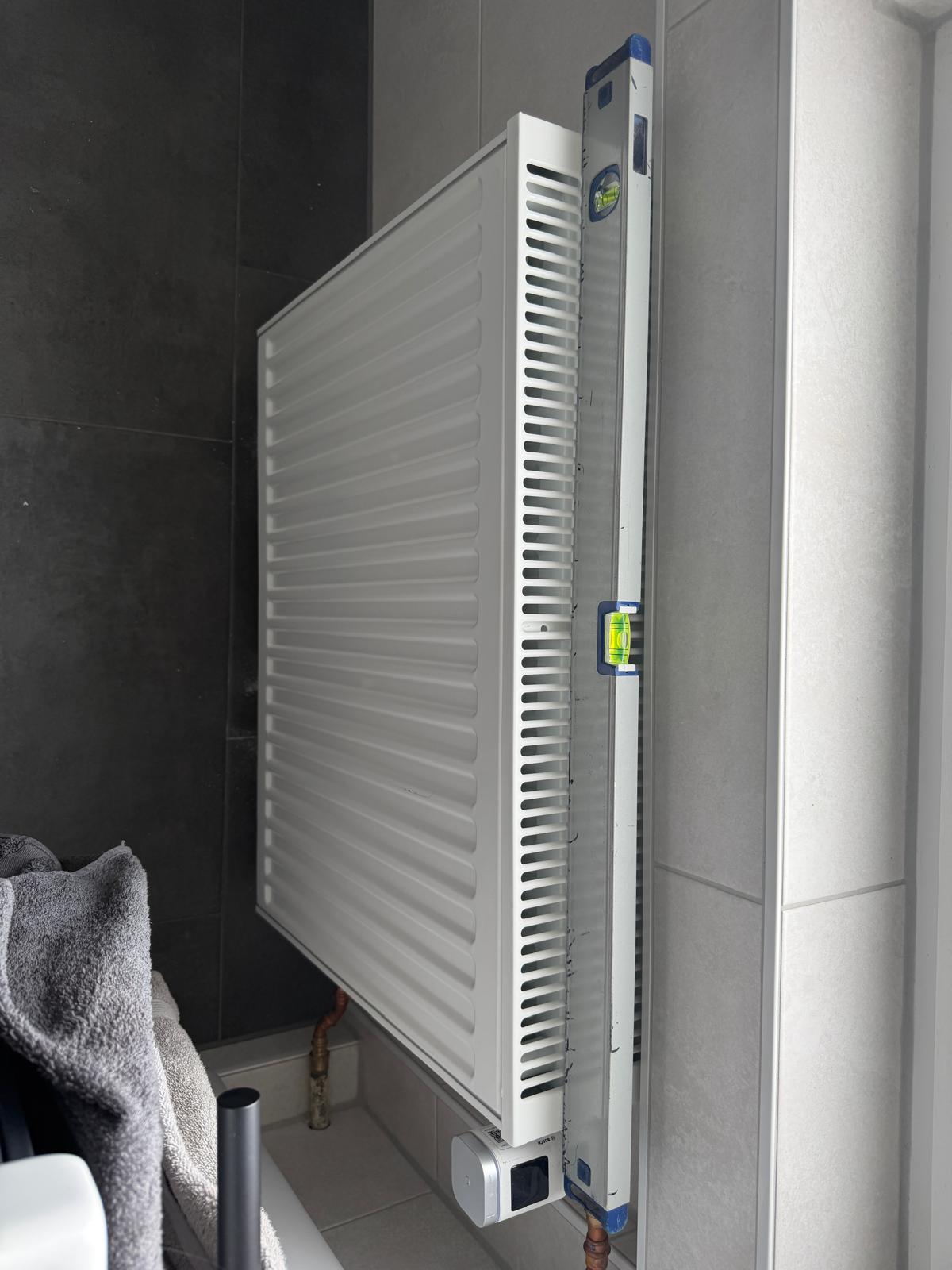 Flachheizkörper an einer gefliesten Wand mit Wasserwaage und elektronischem Thermostat