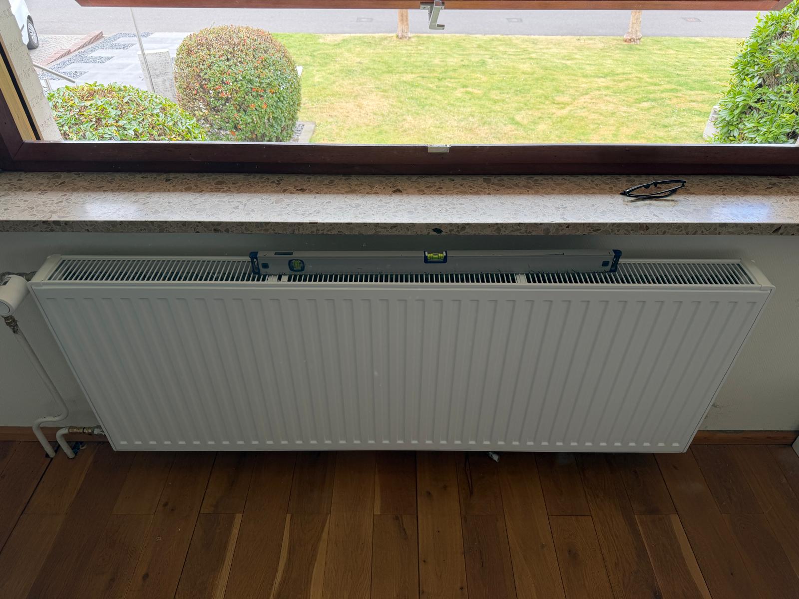 Von EcoConstruct montierter Heizkörper unter einem Fenster mit Wasserwaage zur Ausrichtung
