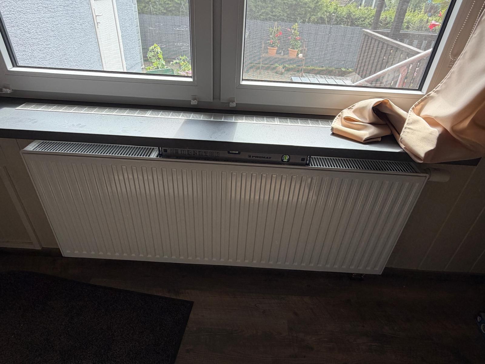 Breiter weißer Heizkörper unter einem Fenster mit Blick auf die Terrasse